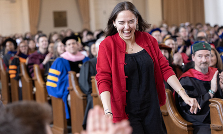 Woman smiling as she walks through a crowded chapel to receive an award on stage. 