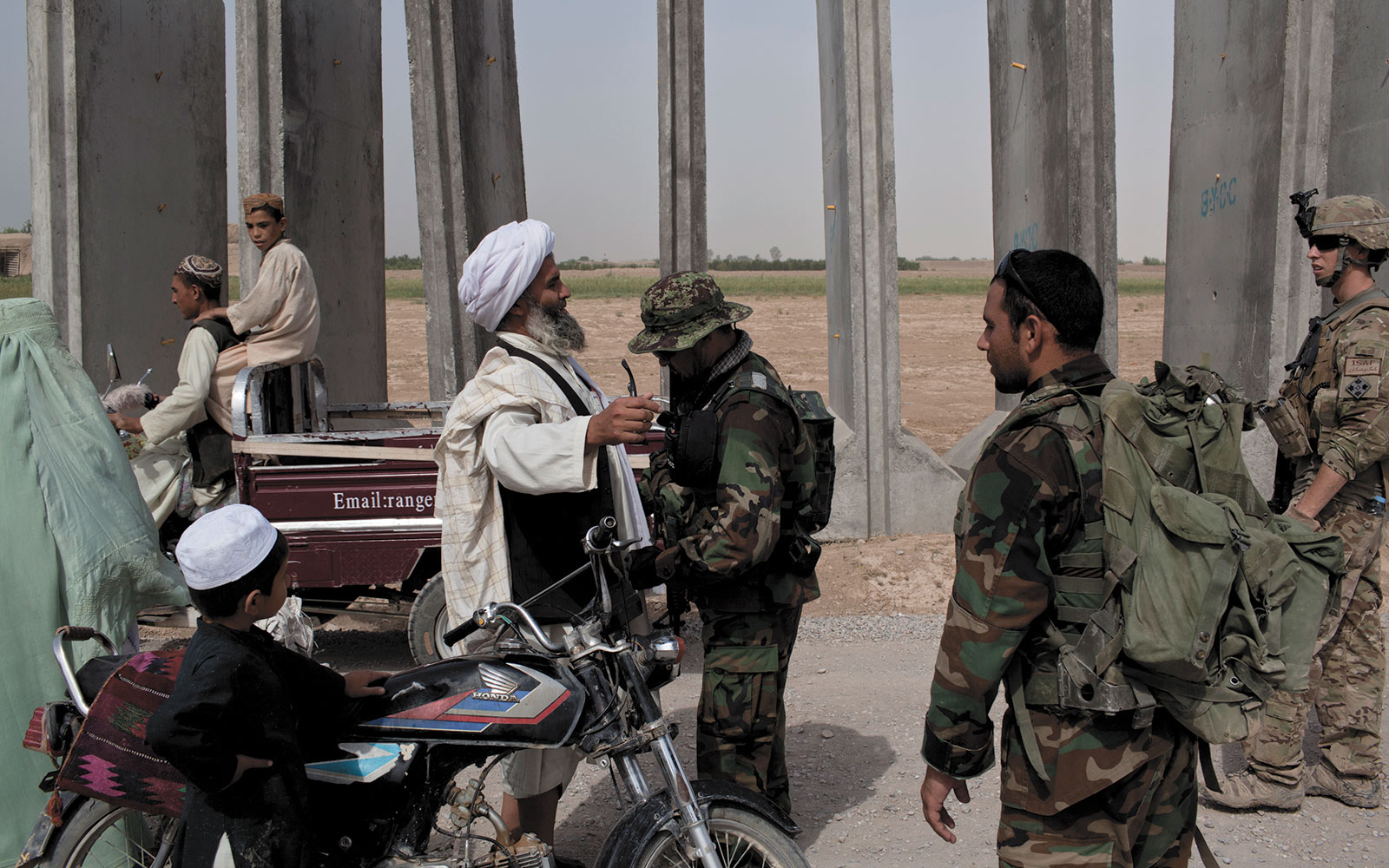 Afghan soldiers search a motorcyclist for weapons, explosives, or insurgent paraphernalia at a traffic control point.