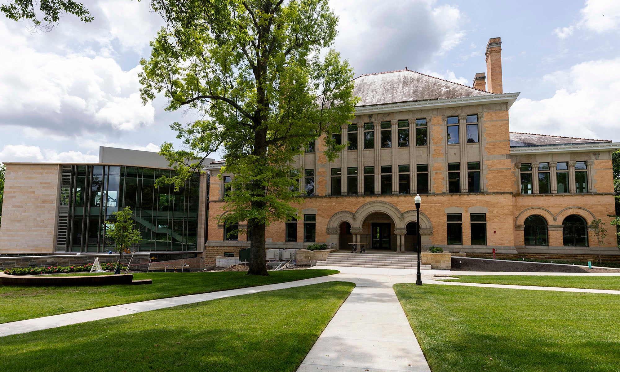 A large brick and glass academic building sits behind a green lawn and sidewalks on a partly cloudy day.