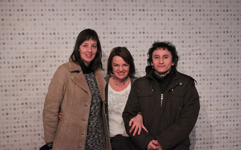 three people smiling in front of wall of dots