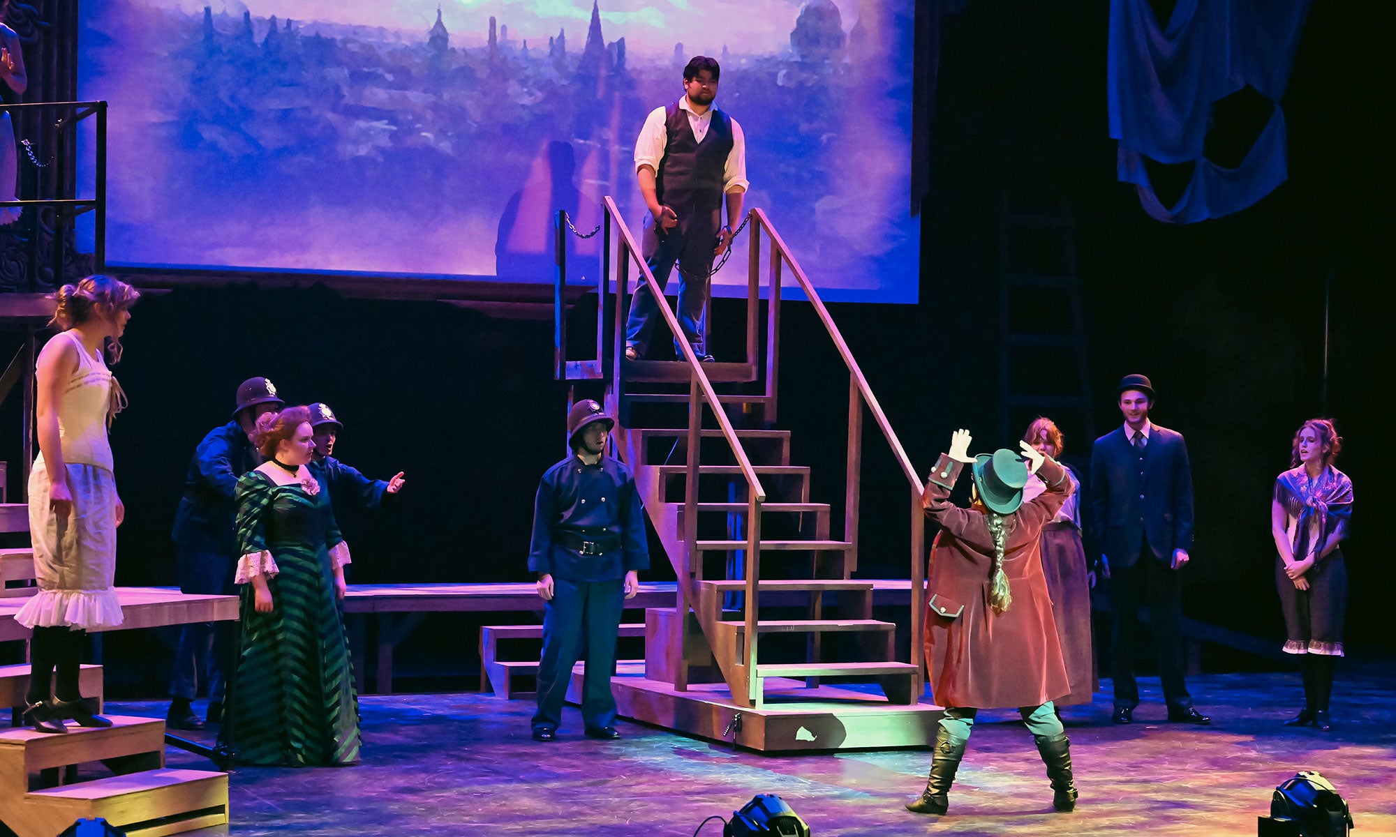 The Balladeer stands at the base of the gallows, taunting Maceath as he stands to be hanged. The police, Mrs. Peachum, Inspector Brown, and several Ladies of Grape Lane watch.