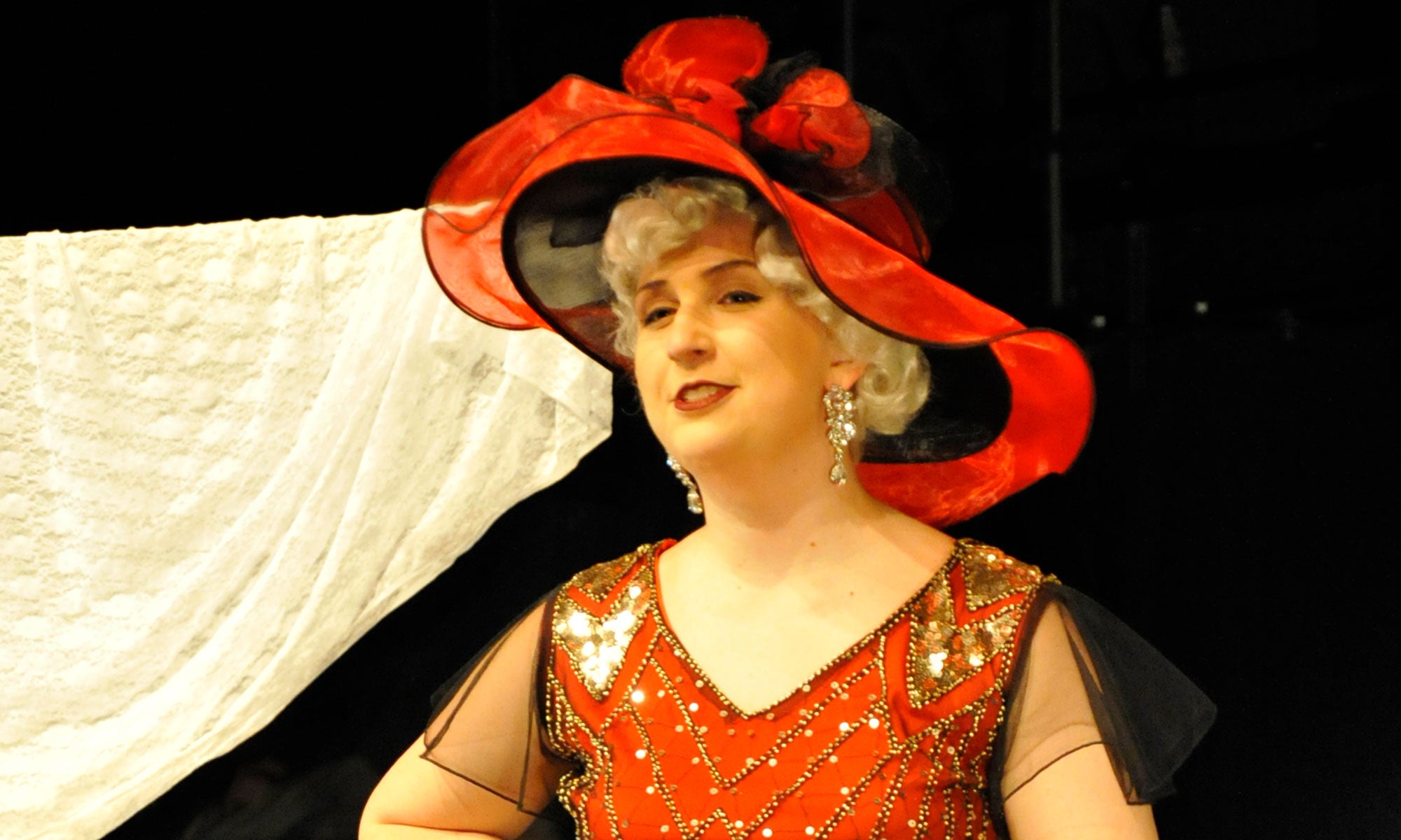 Francesca Mouery in a sparkly 1930s red dress and hat poses as she performs her original solo play Mae West: After Dark.