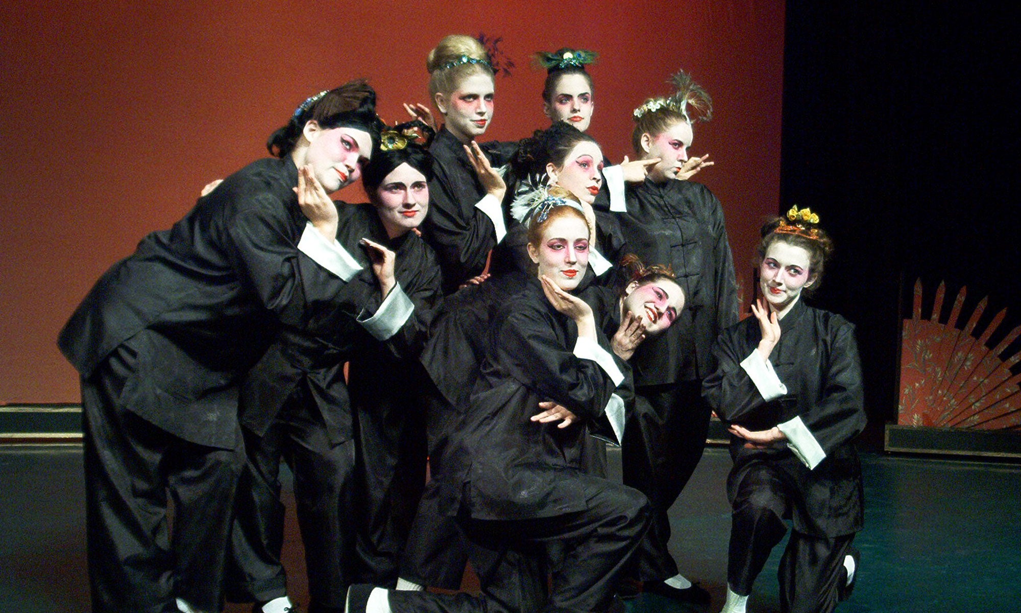 Nine chorus girls in black uniforms and Jingju makeup pose together on stage.