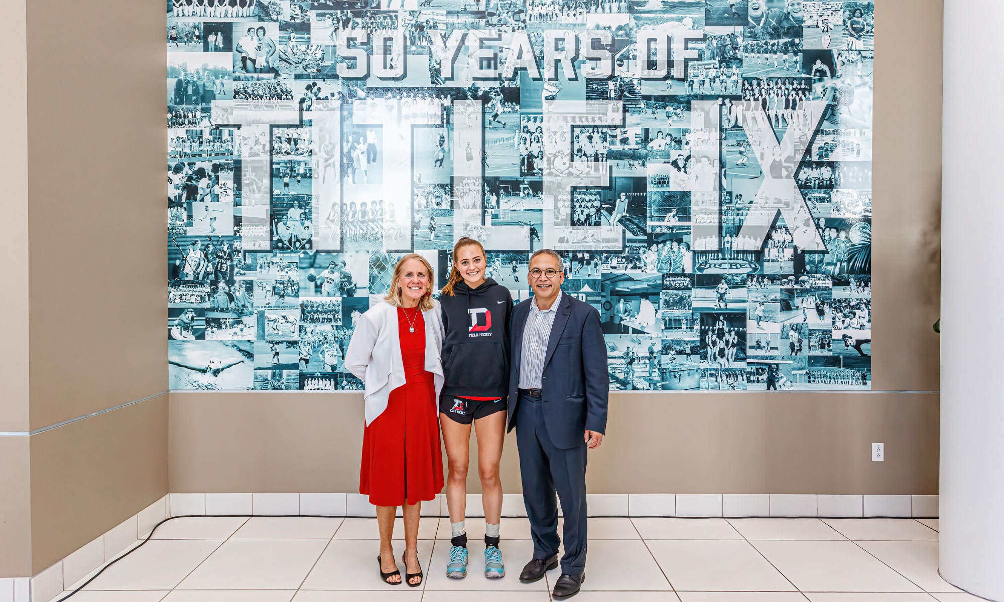 Kate Hinshaw ’24 (center) created the 200-picture collage of Denison female athletes that was transformed into a Title IX mural, which adorns a wall at the Mitchell Center. Hinshaw is flanked by Denison Athletic Director Nan Carney-DeBord and President Adam Weinberg. Photo credit: JR Delgado