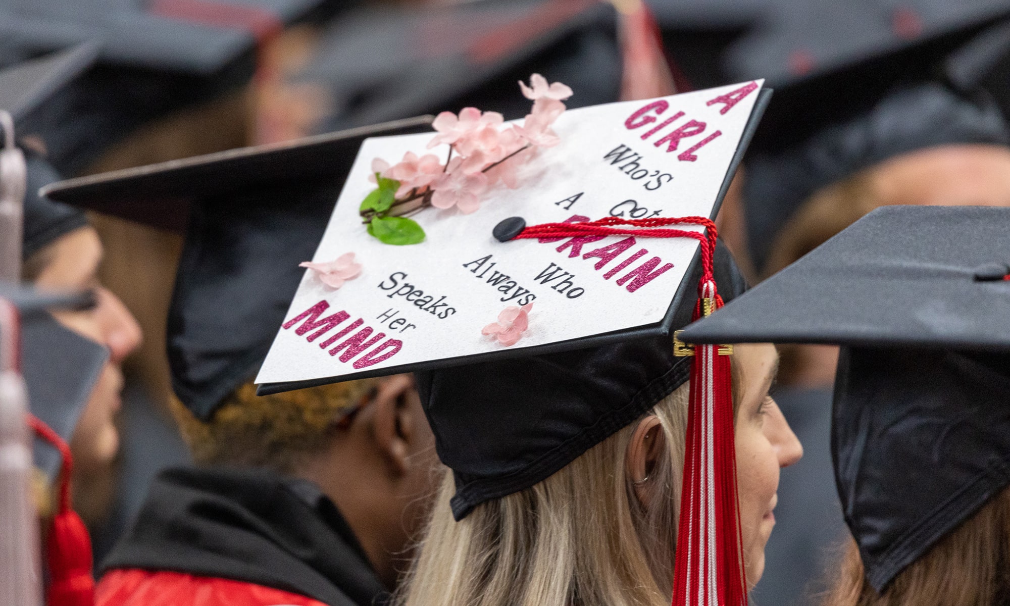 Student graduation cap decorated with flowers that reads 'A girl who's got a brain who always speaks her mind'