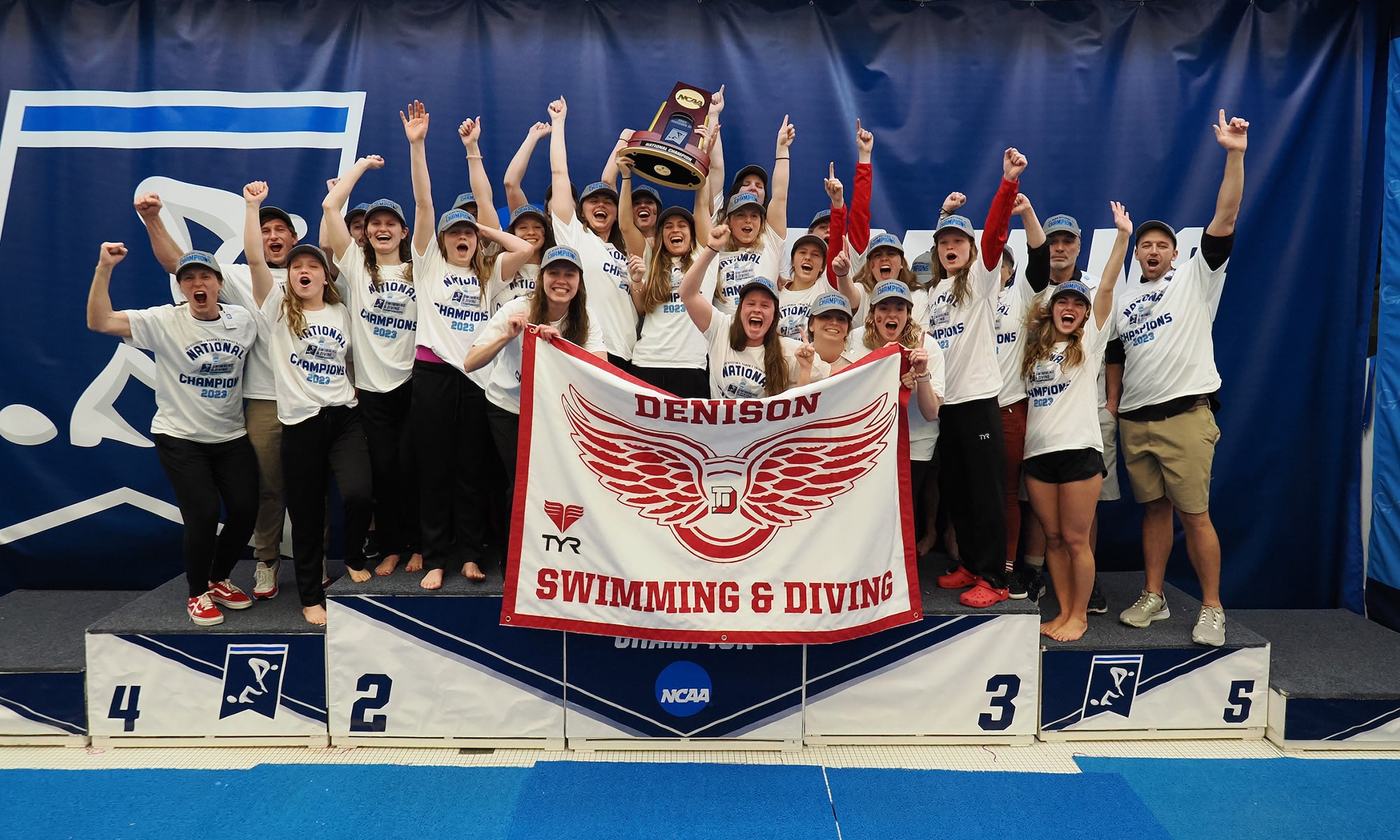 2023 Denison swim & dive team standing on the podium holding a trophy and a flag