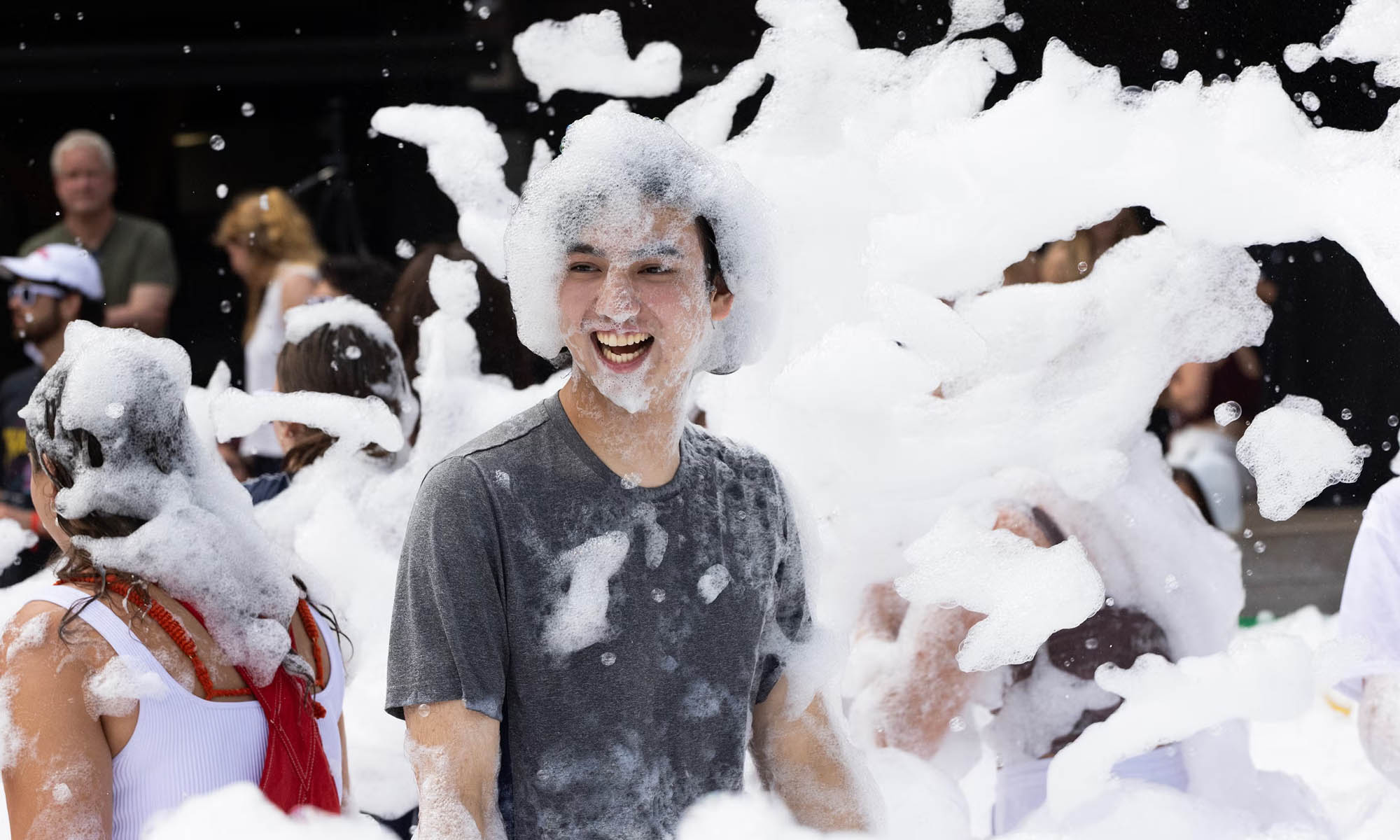 A student covered in giant soap bubbles laughs.