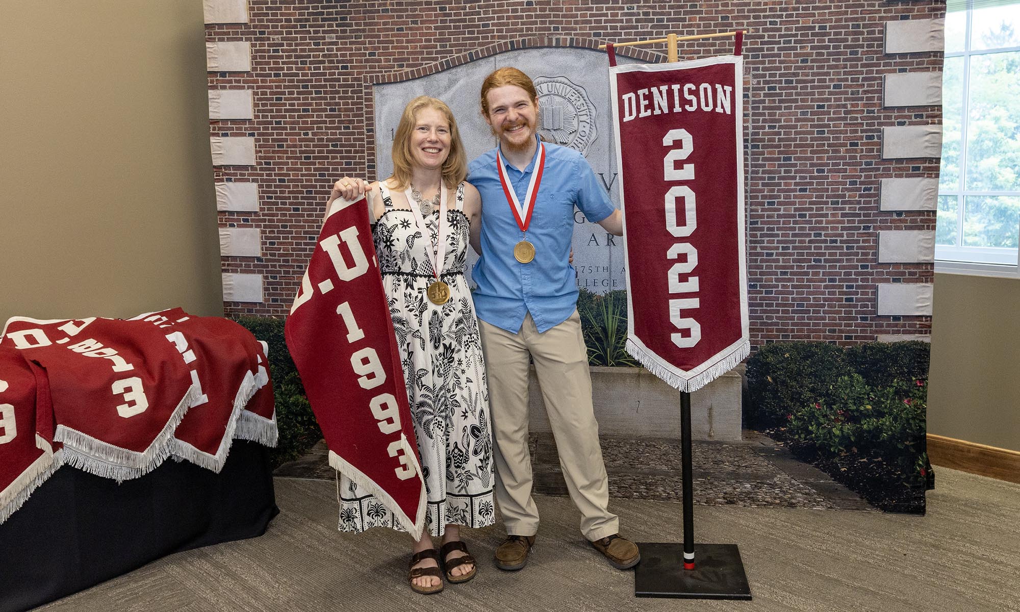 Photo of Tanya Harman Chartier ’93 with her son Noah Chartier ’25 holding class banners for their respective graduation years.
