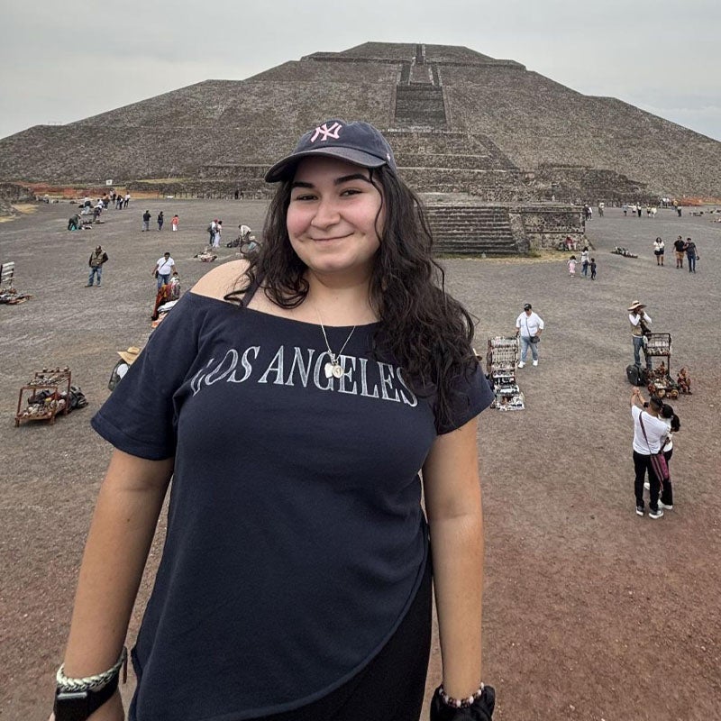 Alyssa Contreras A woman in a black "Los Angeles" tee shirt and New York Yankees baseball cap stands in front of a Mayan pyramid in Mexico.