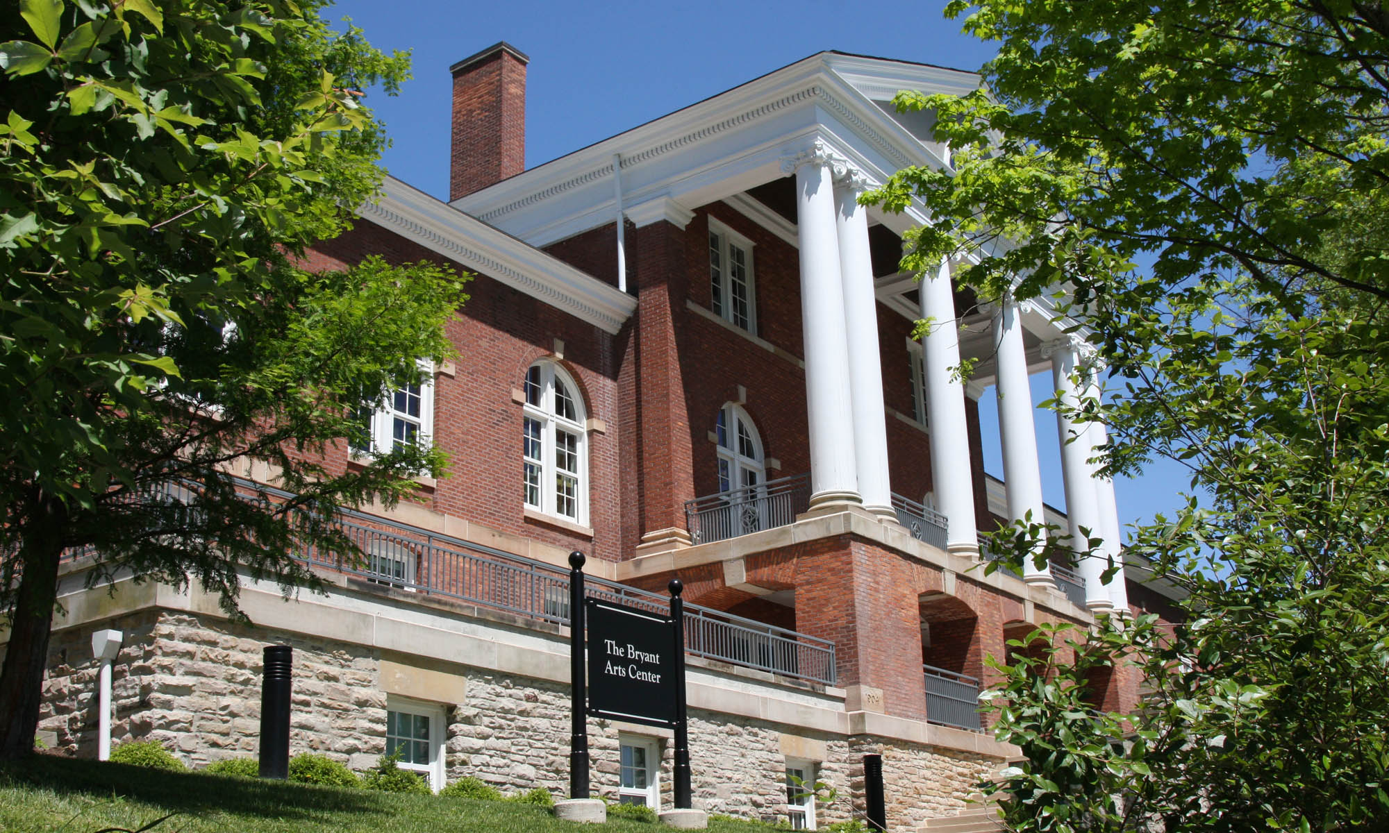 An expansive brick and stone Jeffersonian Federal Revival style building in brick and stone with large white columns along the front porch.