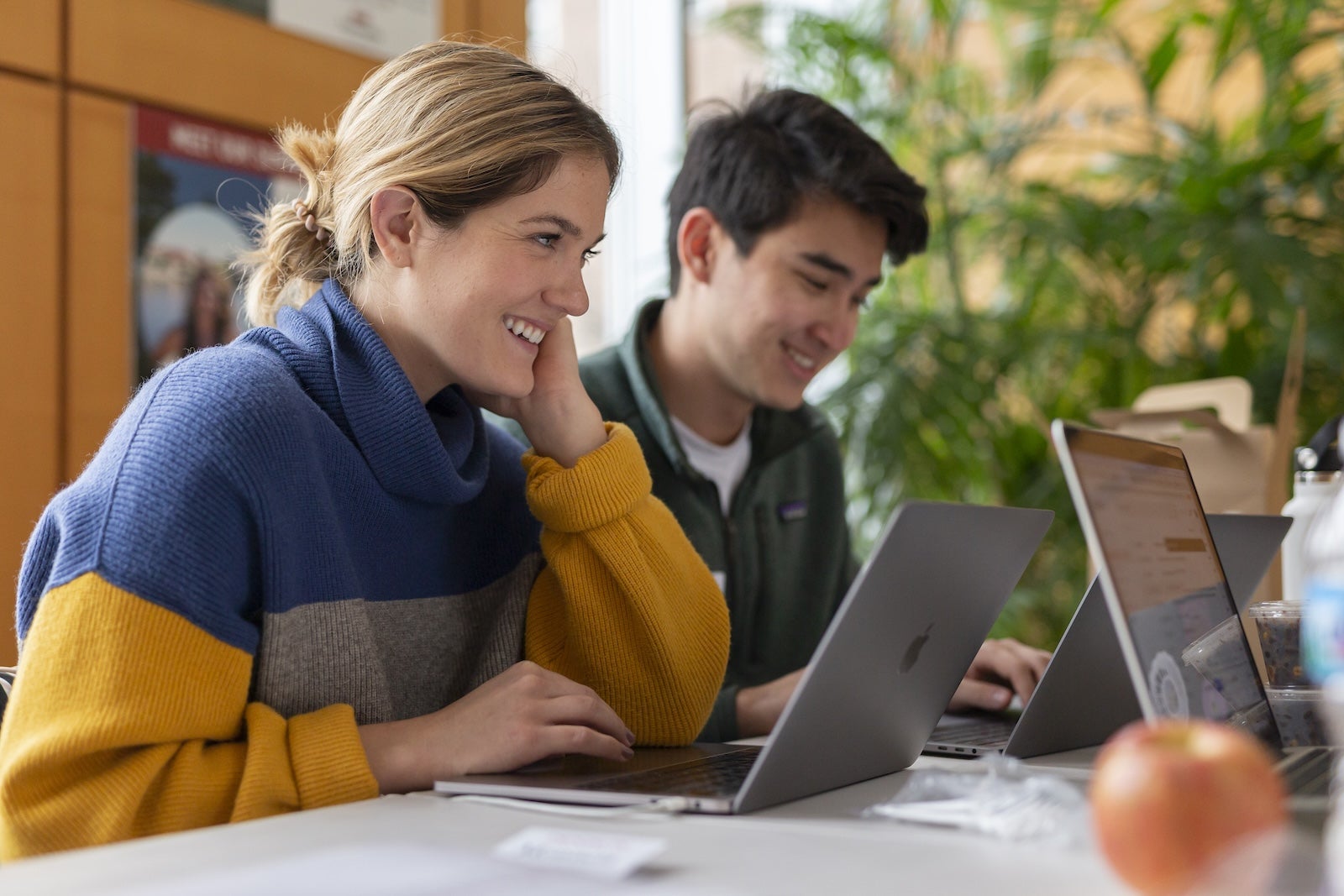 Two students smiling and working on laptops at a table