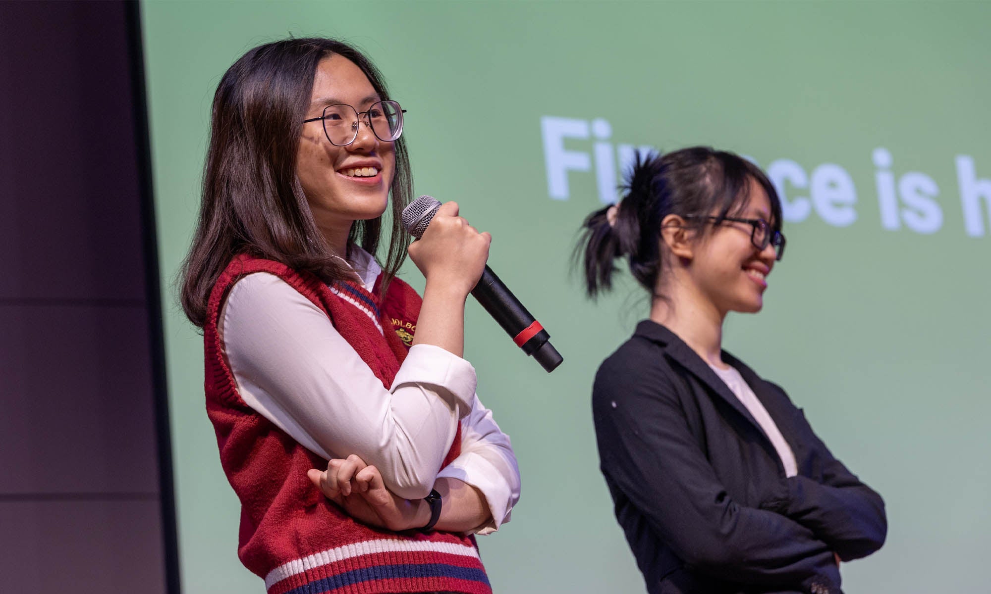 Two students in business wear stand on a stage delivering a presentation.