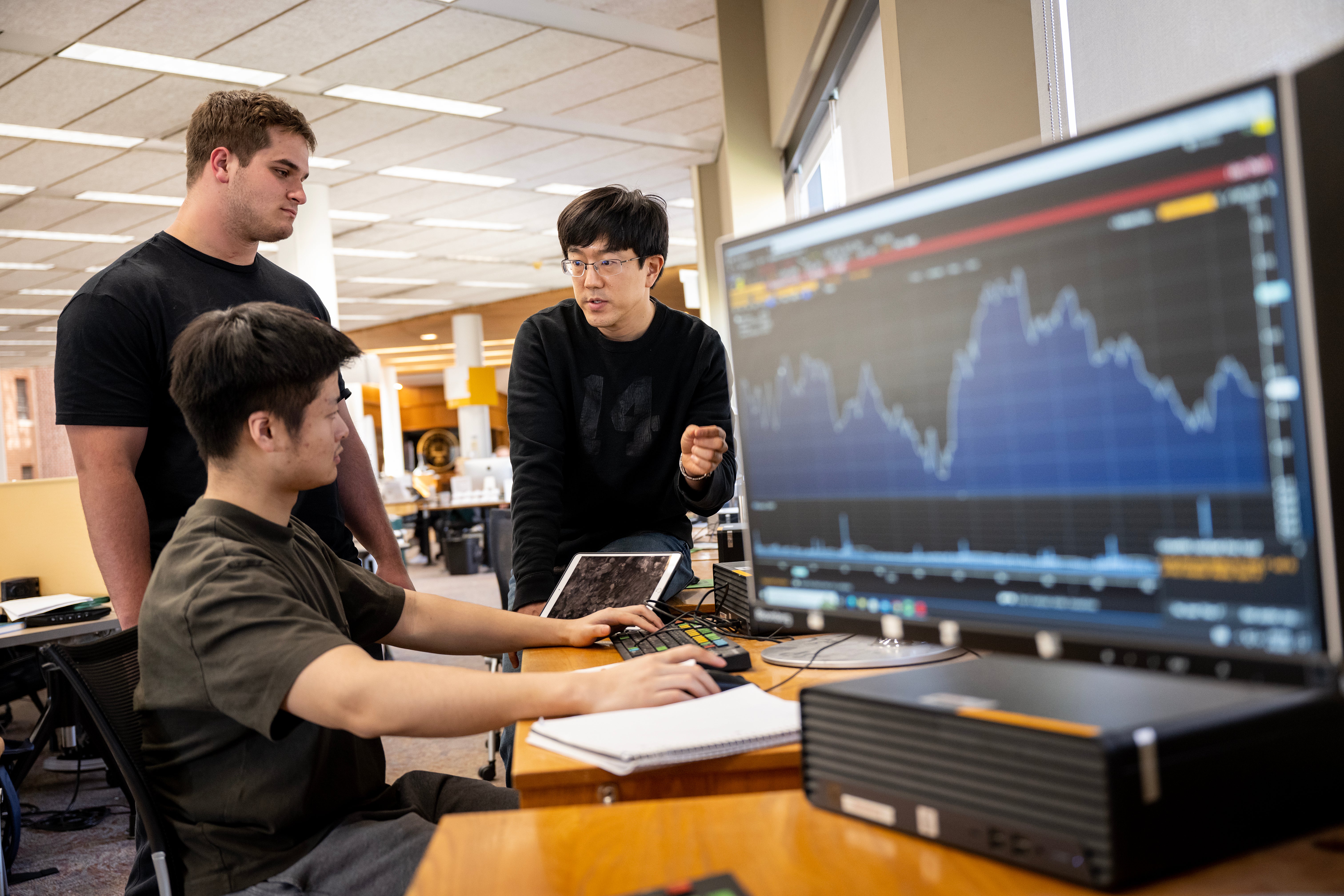 Professor and students discuss data, with a large computer screen displaying a chart