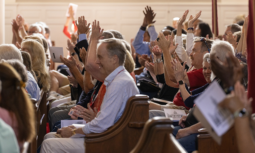 The rows of Swasey Chapel filled with alumni, raising their hands responding to a question during a presentation.