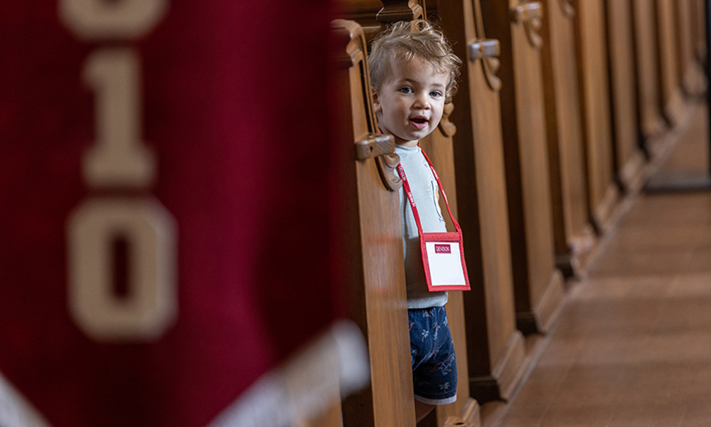 A young boy — a future Denisonian? — peeks out from between the pews in Swasey Chapel; a class flag for the Class of 2010 partially visible in the foreground.
