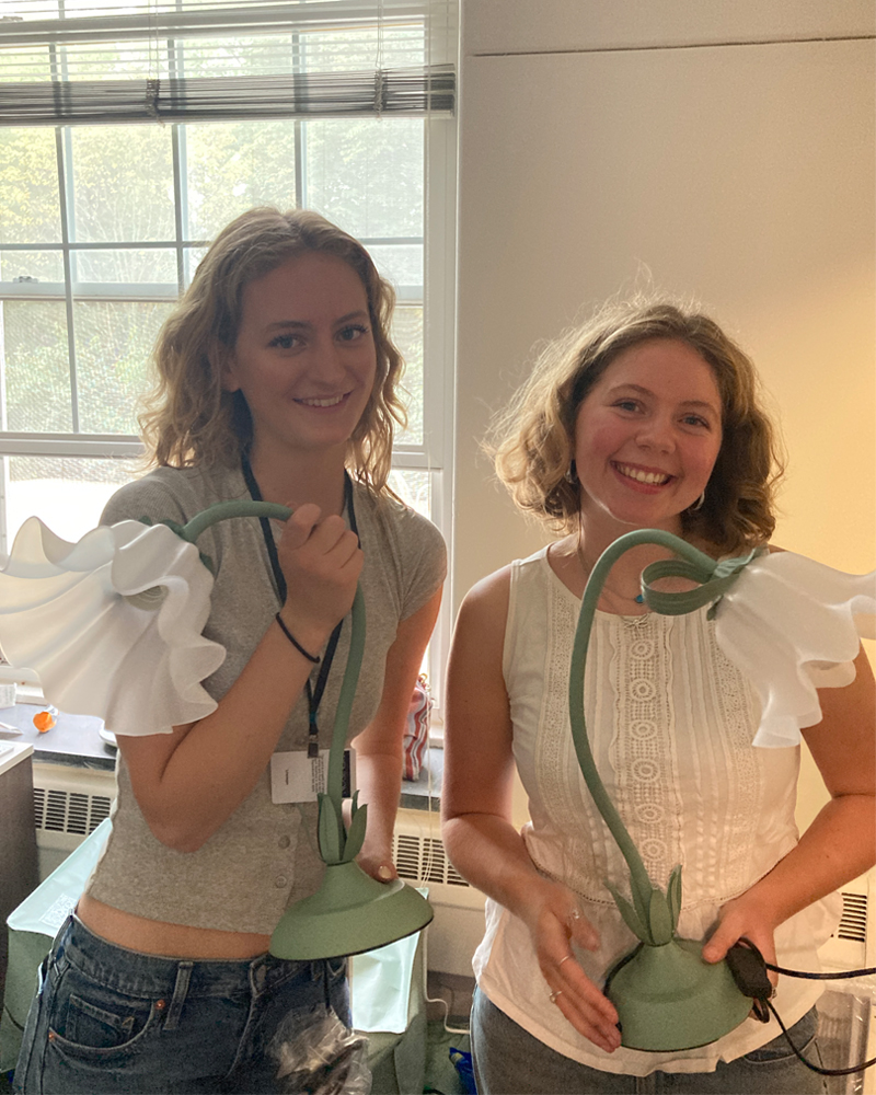 Two Denison students pose for a photo with their matching lamps in their dorm room.