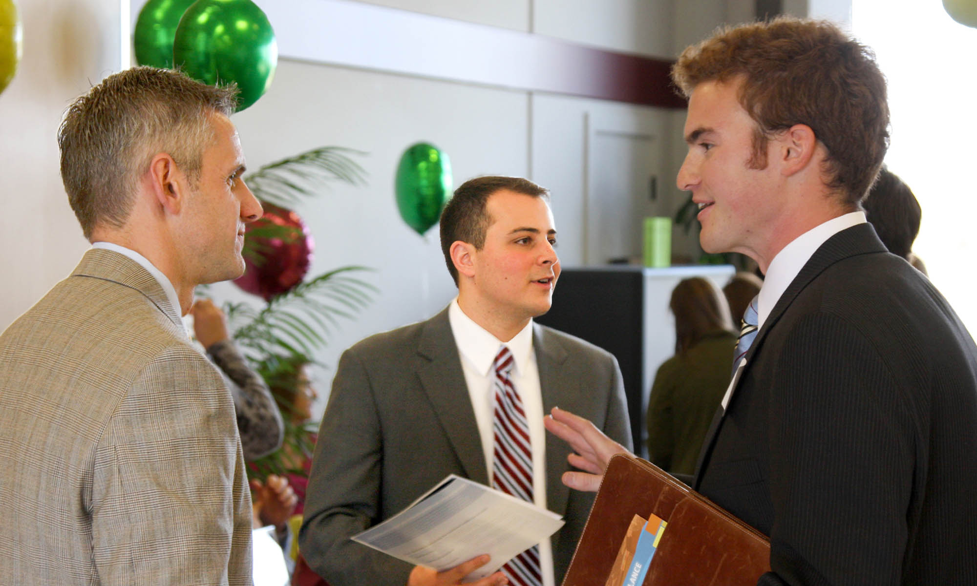 Two students in business suits speak with a business professional.