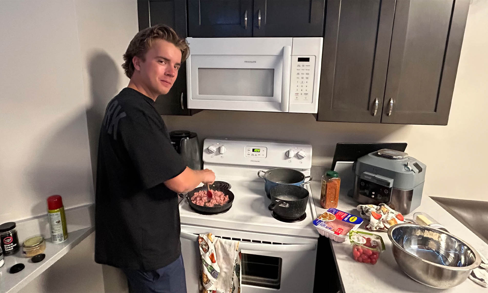 Photo college student Jonathan Westfall ’27 cooking at a stove in an apartment kitchen.