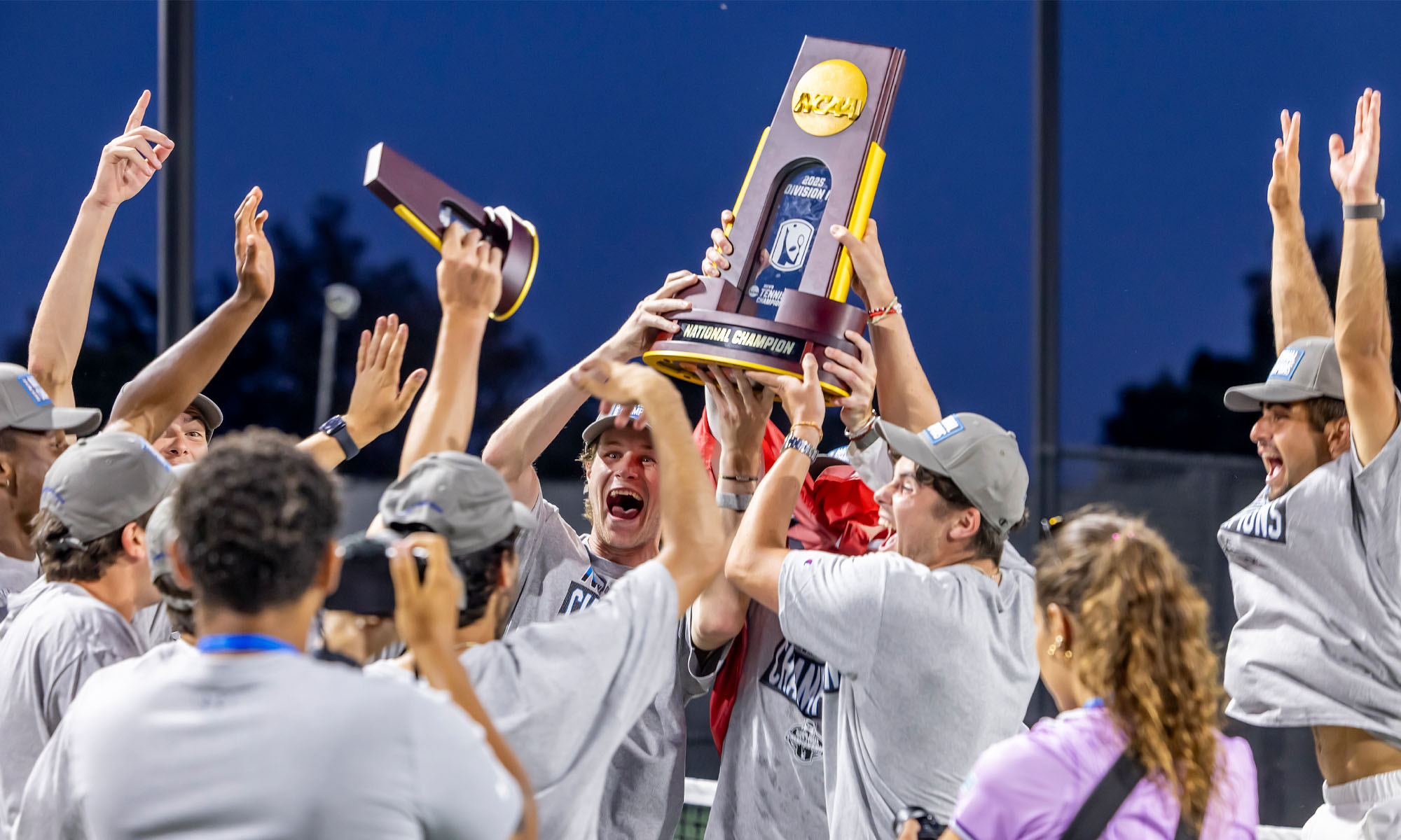 The Denison Men's Tennis team grouped together holding their NCAA championship trophy aloft.