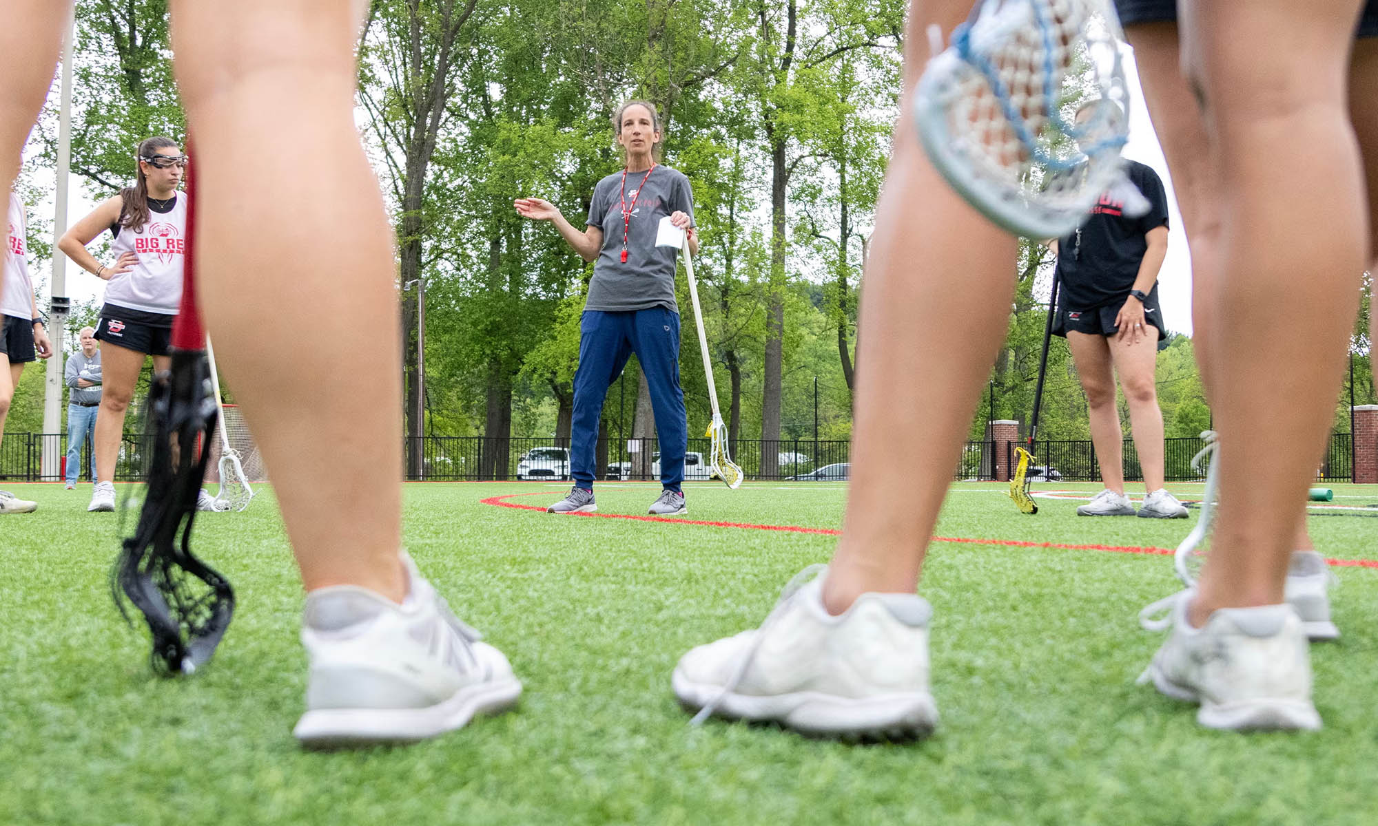 Women's lacrosse players at practice listening to their coach.