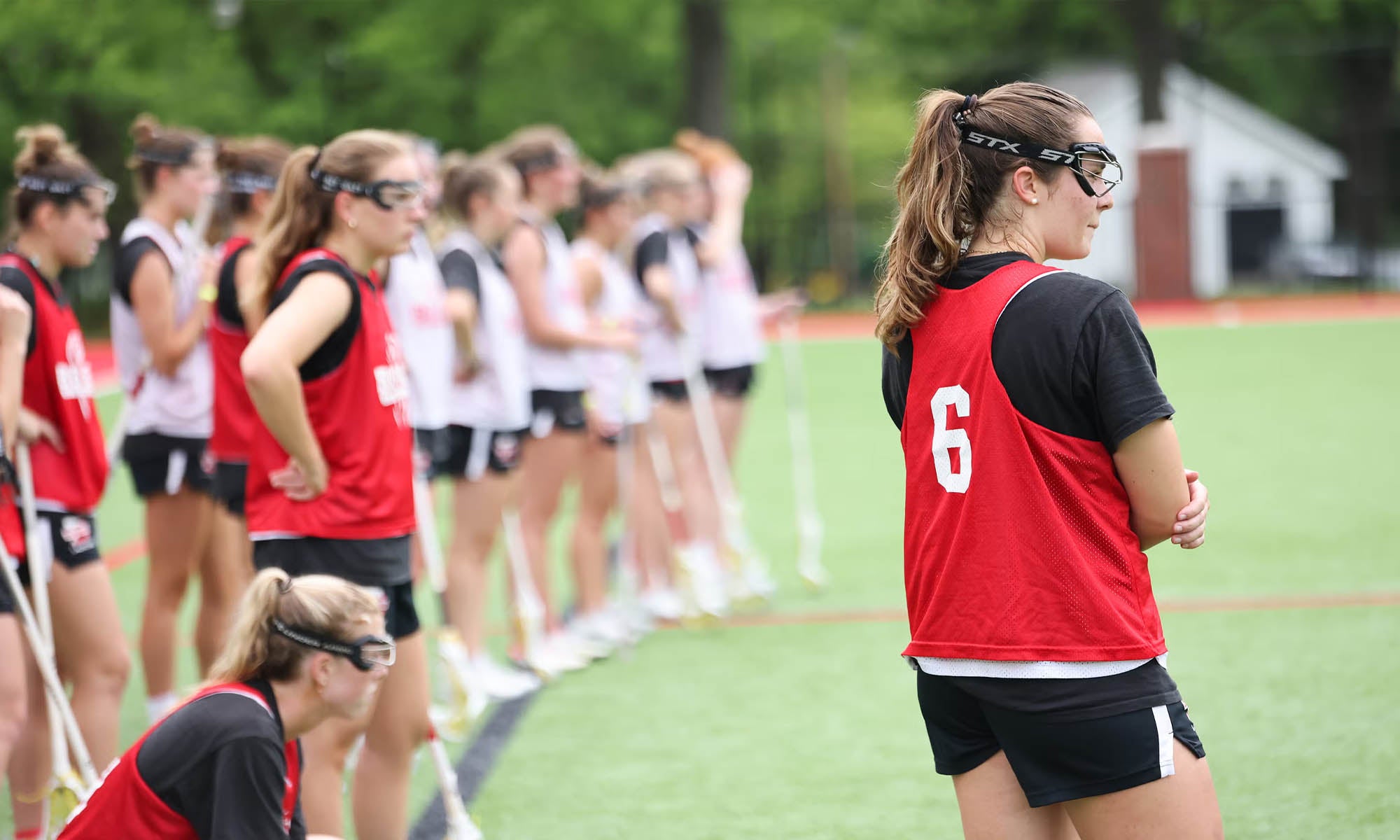 Women's lacrosse players at practice watching from the sidelines.