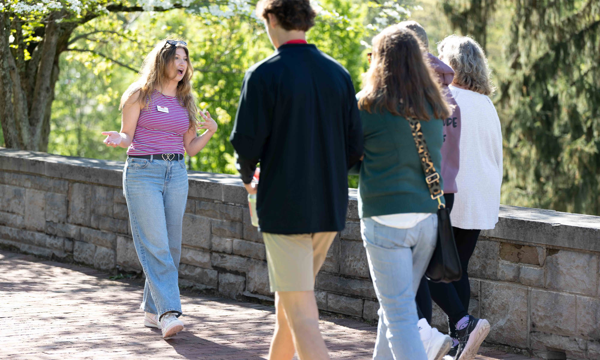 A student in jeans and a red and white striped shirt leads a campus tour.