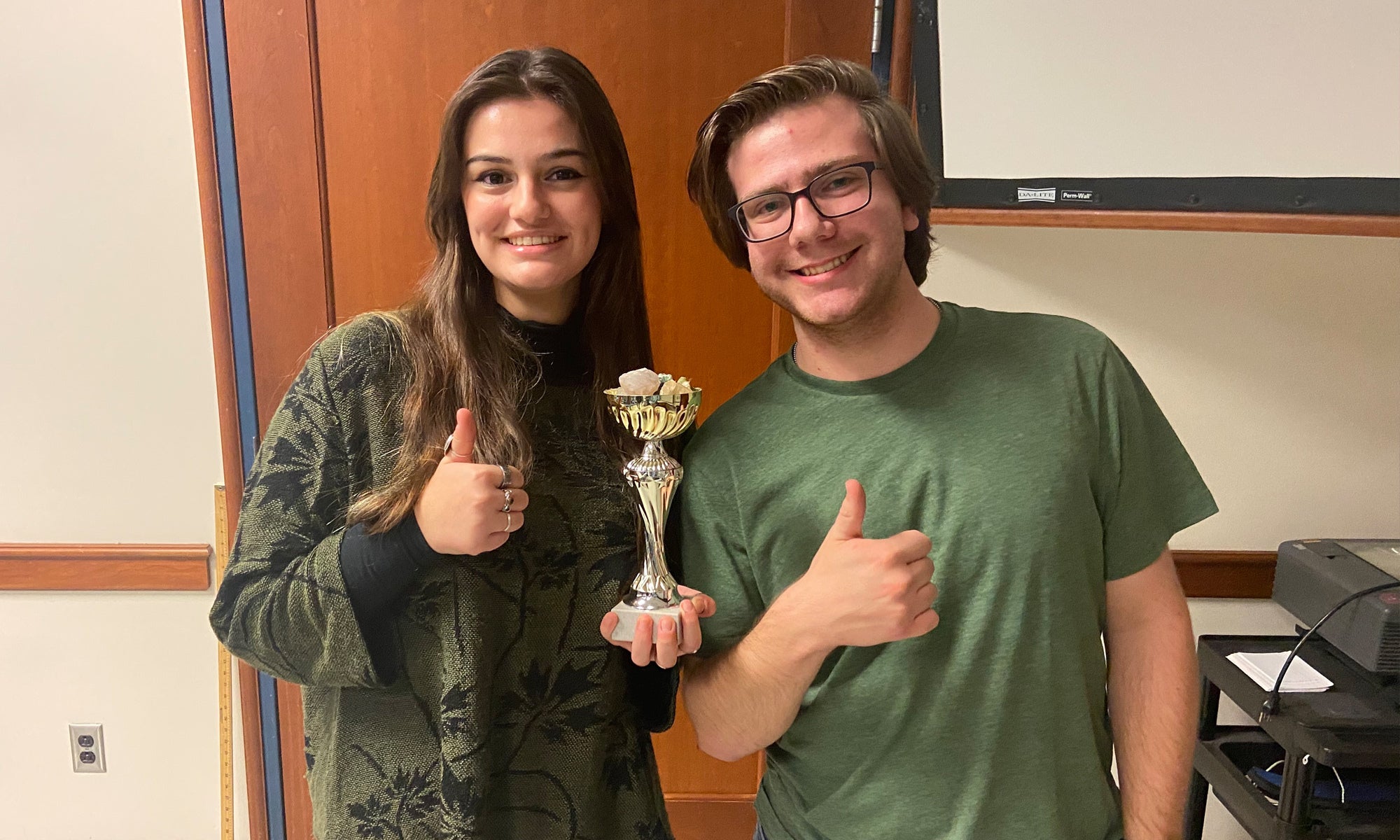 Two students pose together with a trophy giving a thumbs-up sign.