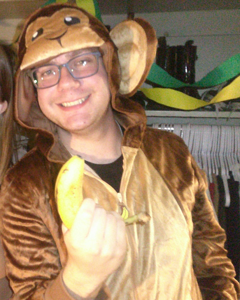 A college student with glasses in a monkey "onesie" costume at a party.