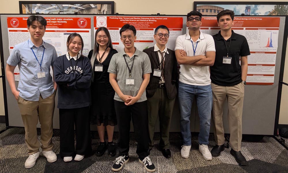 Mathematics students pose for a photo in front of a panel of presentation posters.
