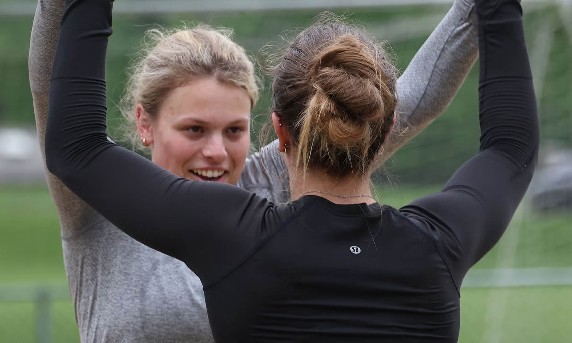 Two students congratulate each other with a double high-five on a sand volleyball court.