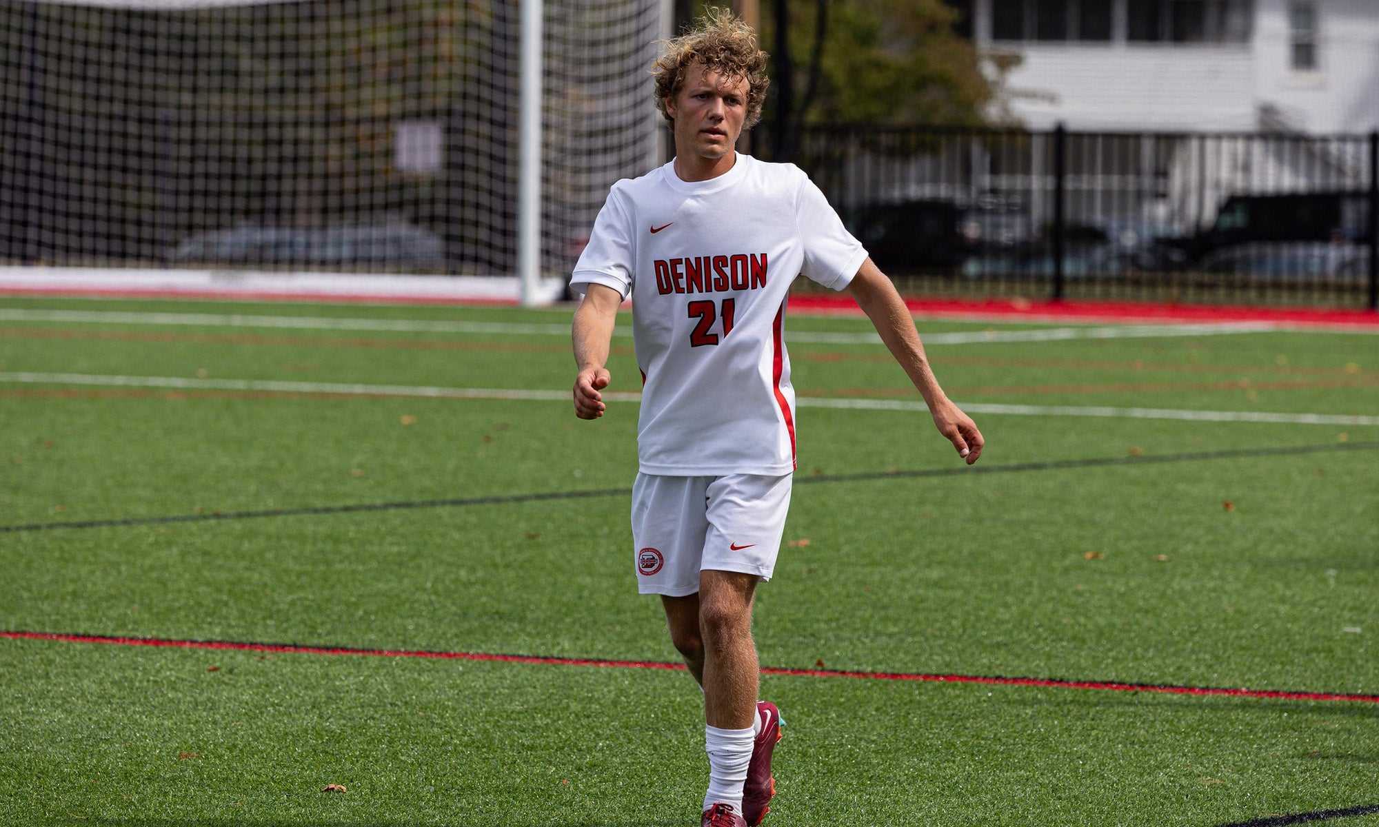 A college soccer player in a white uniform in play on a soccer field.