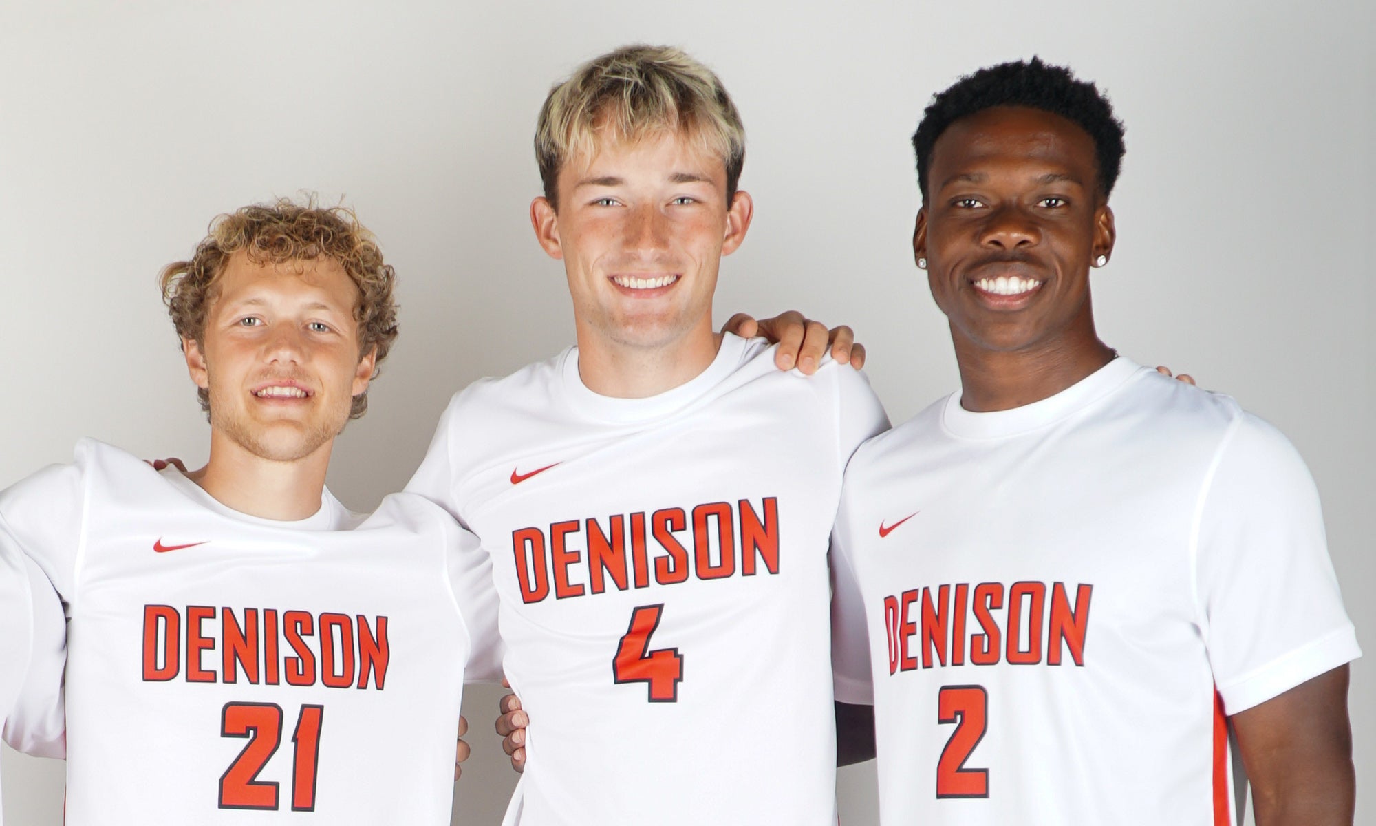 Photo of three college soccer players in  uniform smiling for the camera.