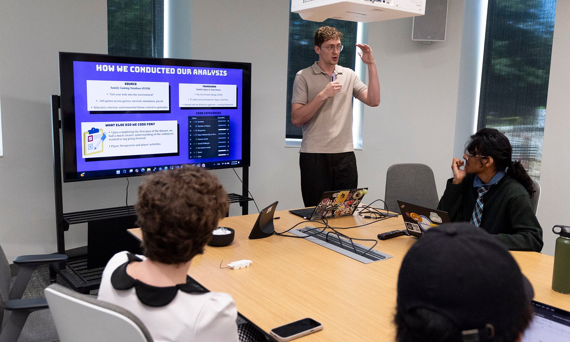 A man presents data analysis slides on a screen to three seated colleagues in a conference room.