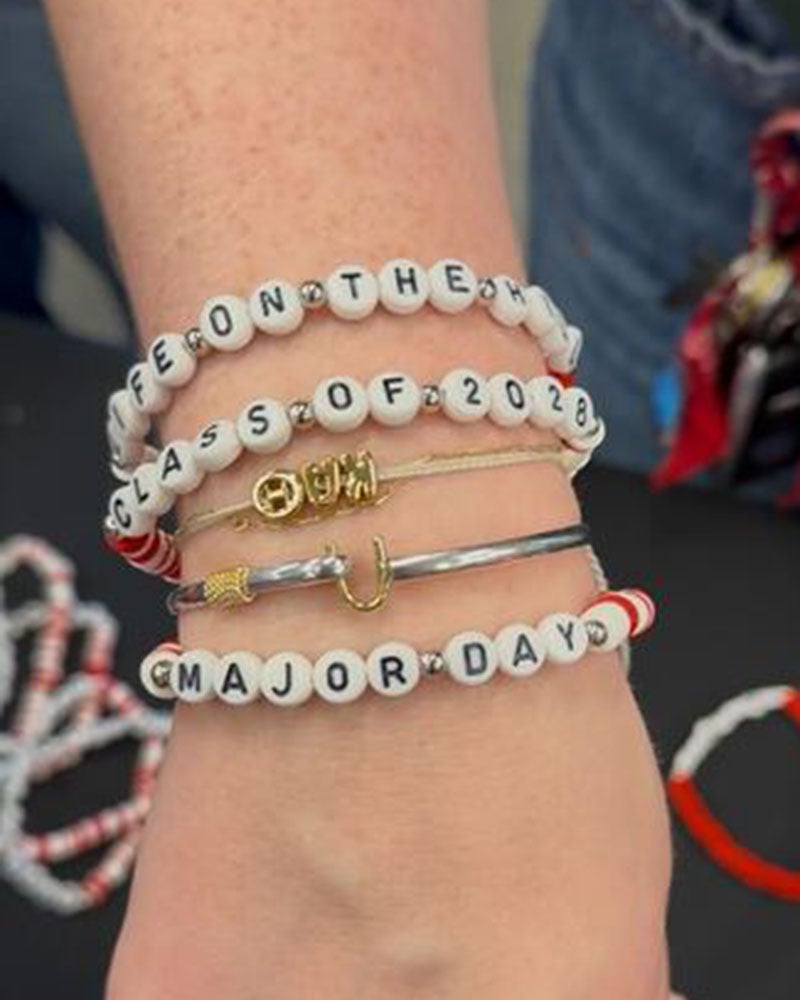 Close up of a person's wrist wearing beaded bracelets spelling out “Life on The Hill,” “Class of 2028," and "Major Day."