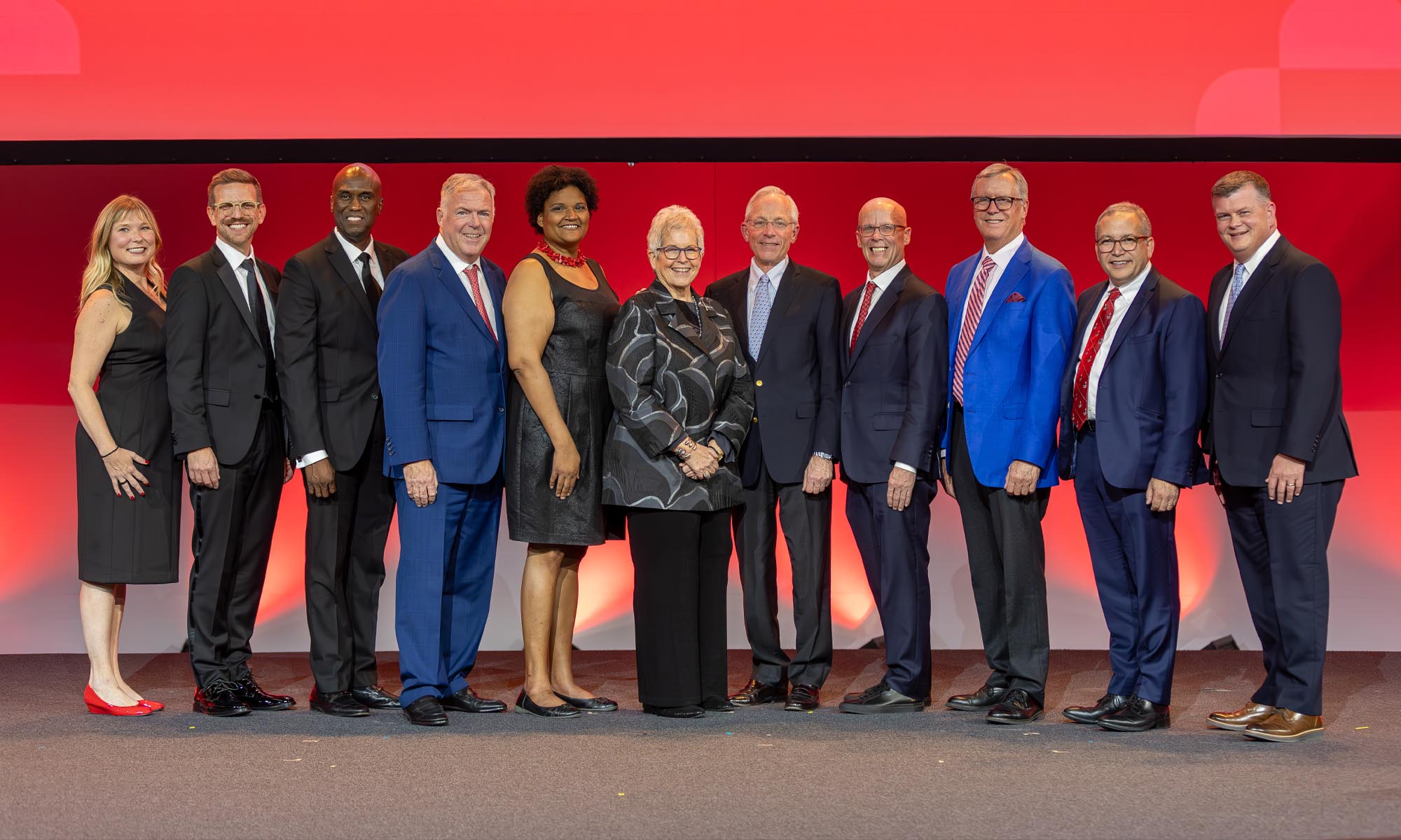 11 people in business and formal attire standing on a stage.