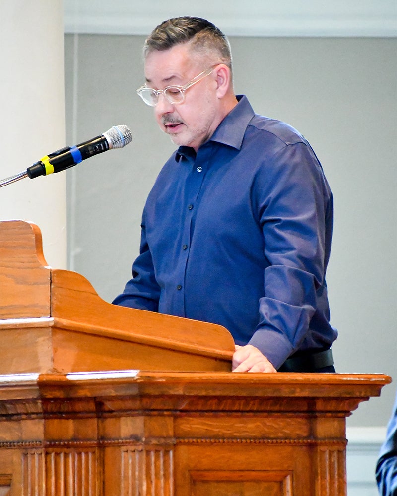 A man in a blue shirt stands at a wooden podium.