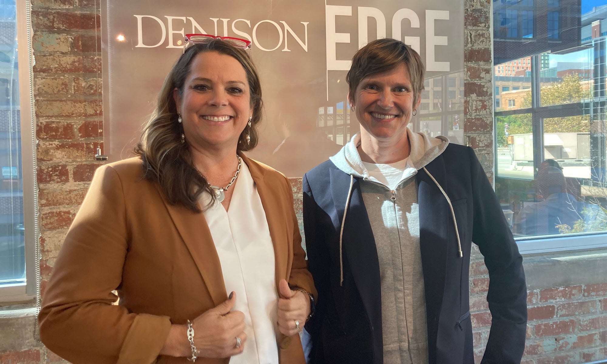 Two women in business wear standing in front of a Denison Edge sign in a modern office building.