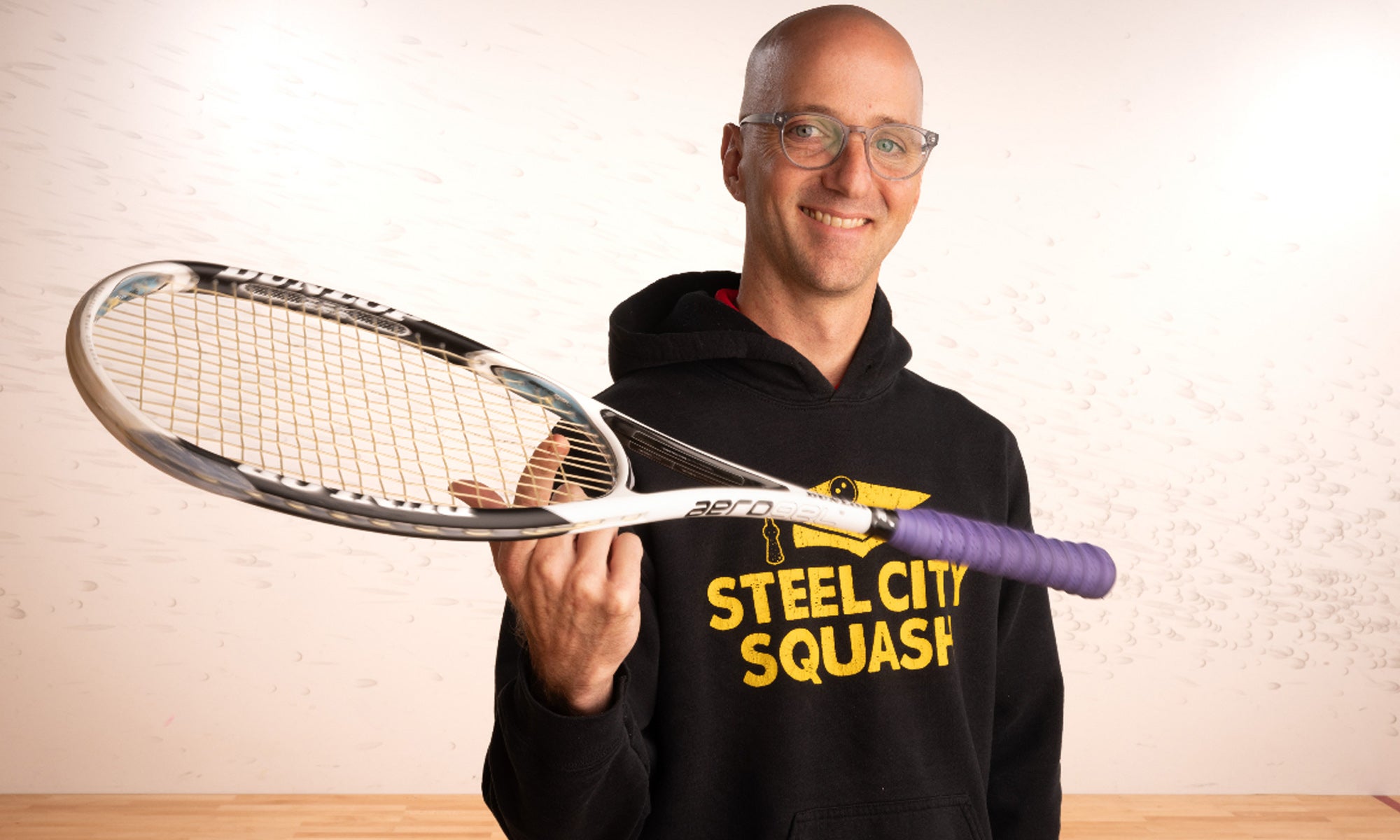 Brad Young ’07 wearing a Steel City Squash hoodie and holding a squash racket.
