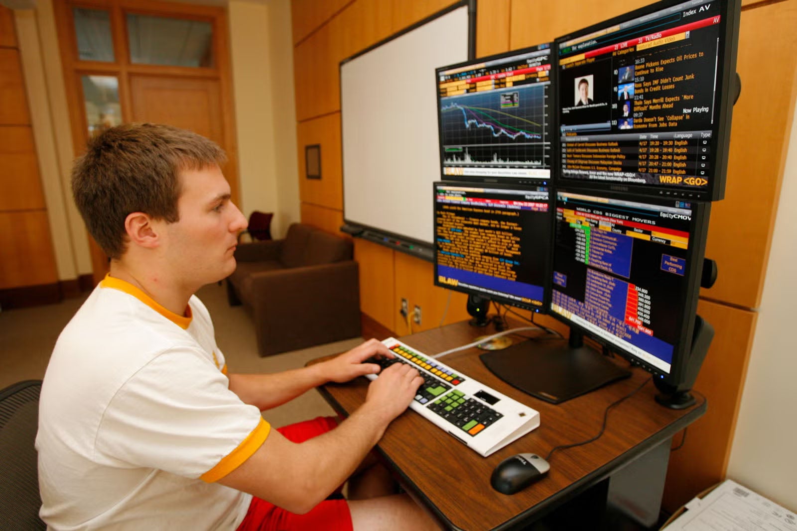A student using a Bloomberg Terminal, comprised of a keyboard, mouse, and four, large computer monitors.