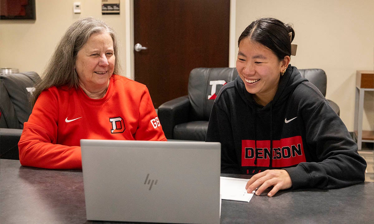 A Denison University faculty member and student sit at a desk reviewing data analytics information on a laptop computer.
