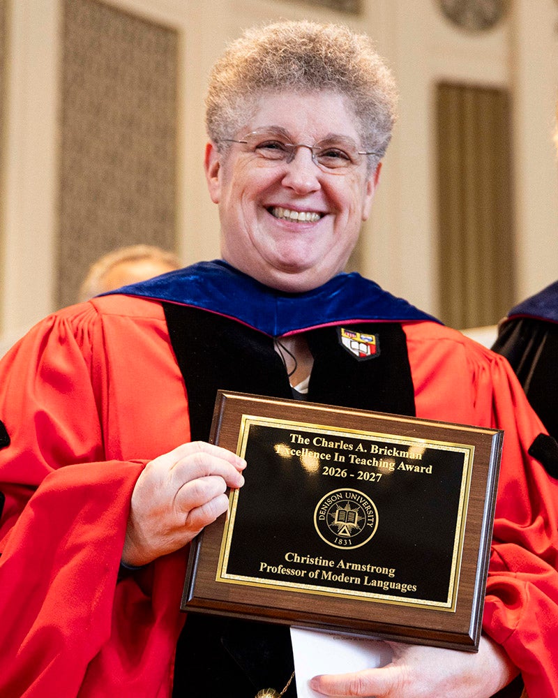 A woman in red doctoral academic regalia holds an award.