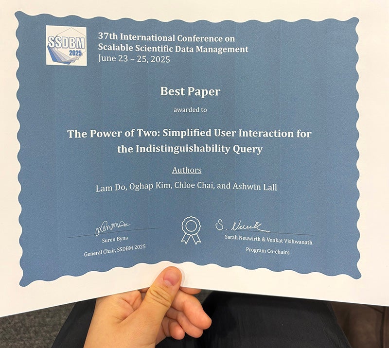 Close up of a hand holding an award certificate from the 37th International Conference on Scalable Scientific Data Management that says "Best Paper" and lists the paper title and authors names.