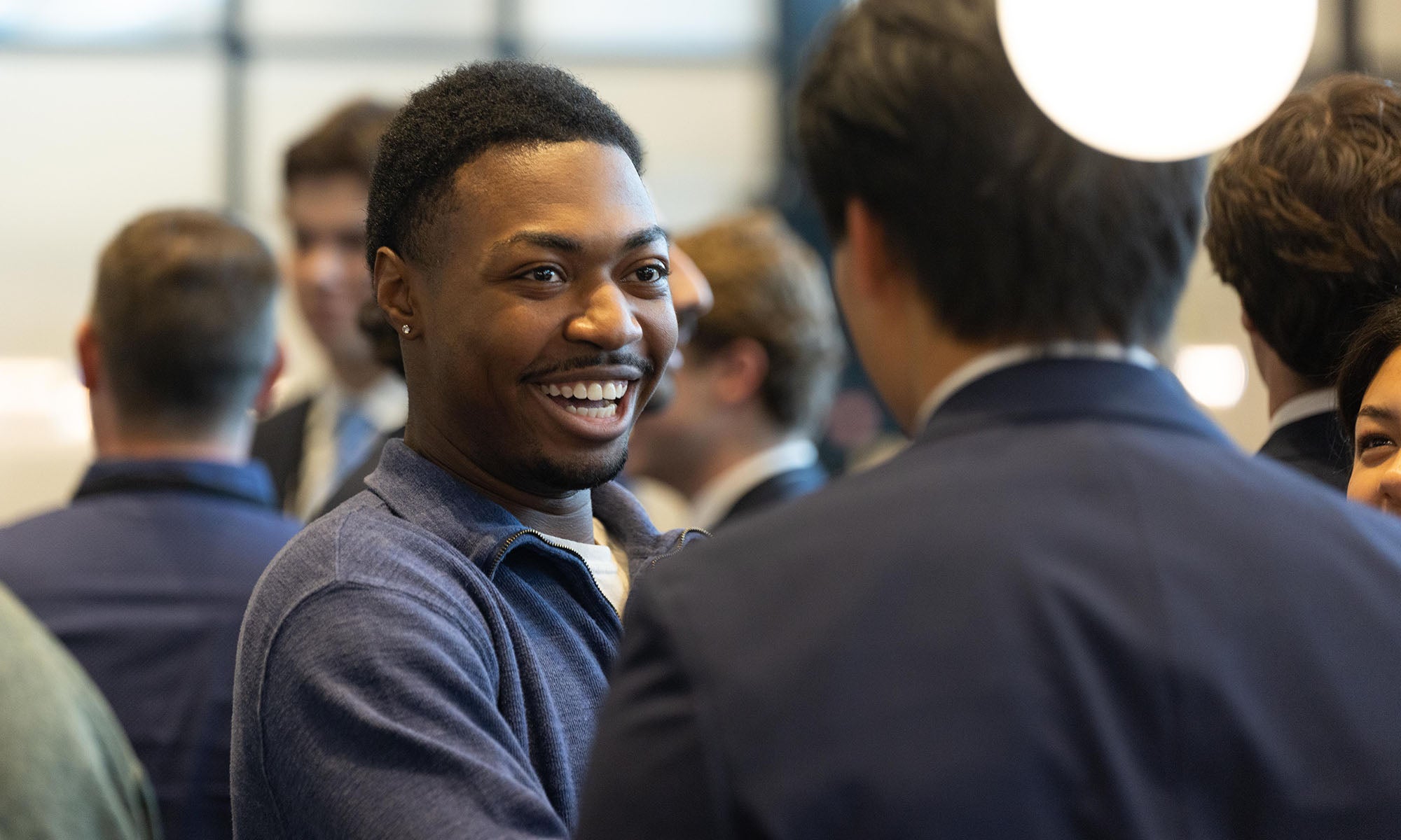 A man smiles while chatting with another man at a business networking event.
