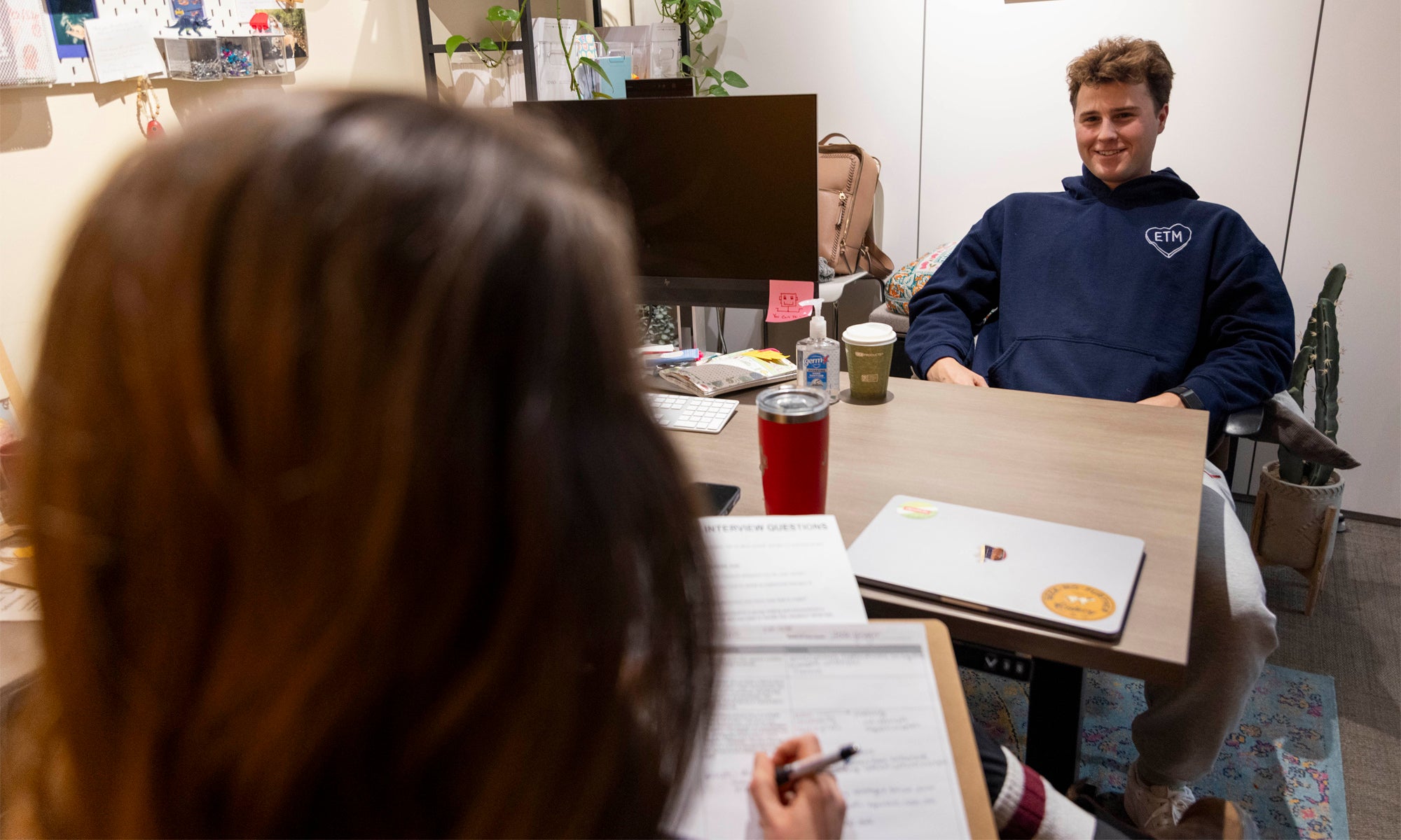 A student sits across a desk from an unseen person in the foreground.