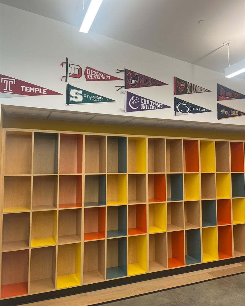 A wall of  colorful shelves divided into a storage blocks with several university pennants displayed above them, including one from Denison University.