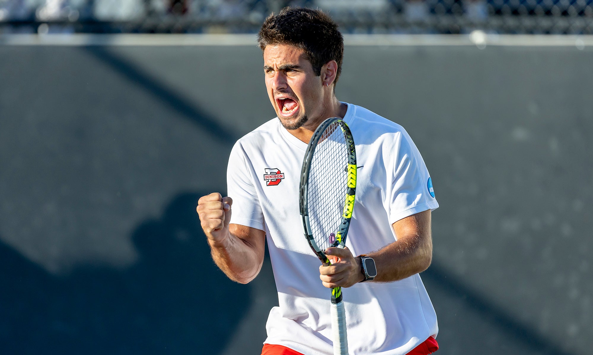 A tennis player holding a racket and pumping his fist celebrates a victory on the court.