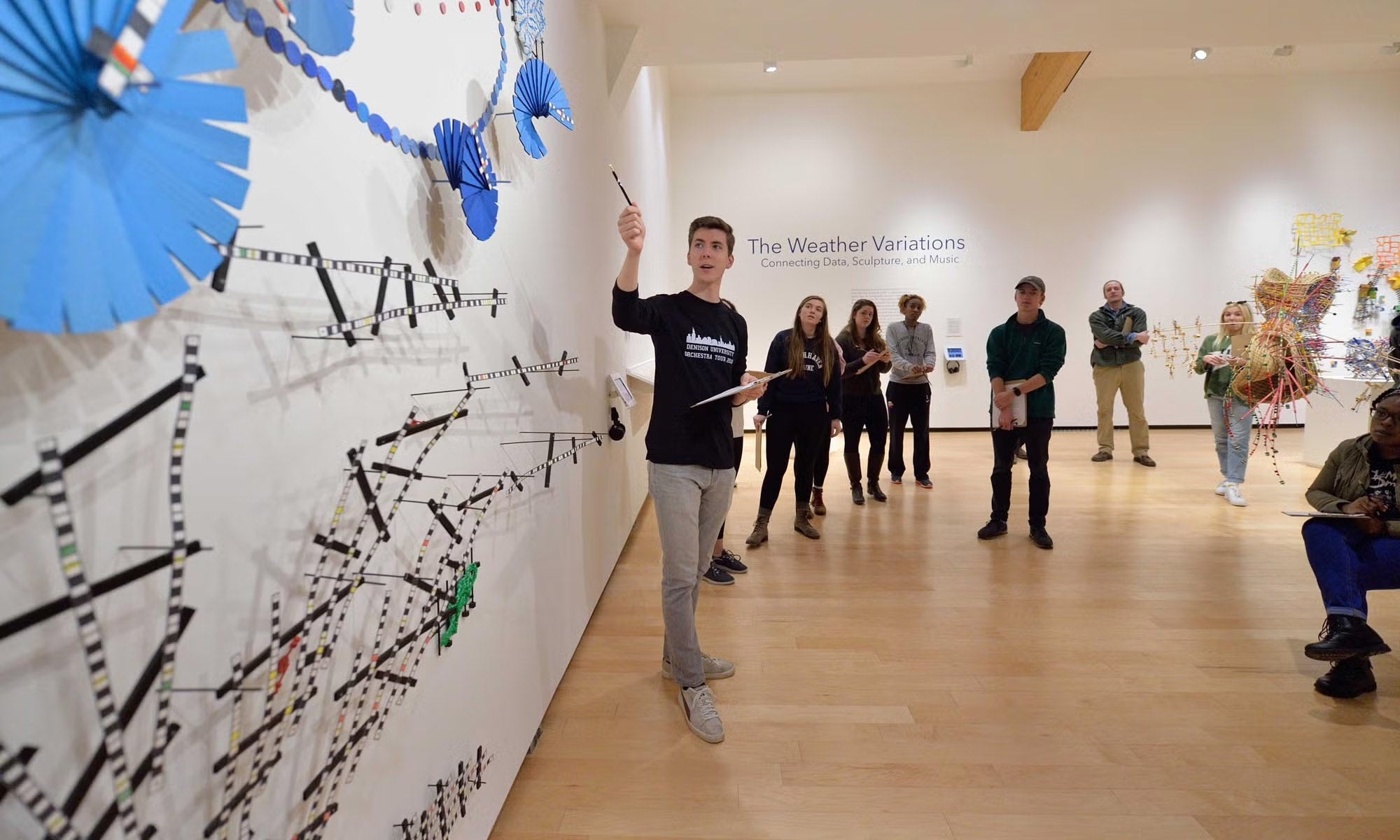A guide leads an exhibition talk to a group of people in a museum gallery space.