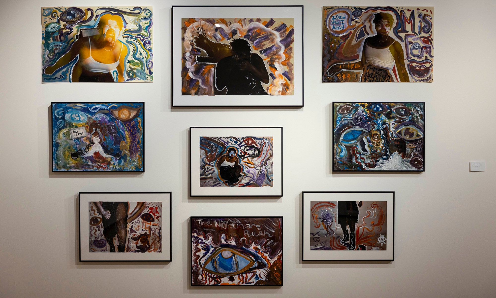 A gallery wall displays nine framed mixed-media artworks from "It Was Never Just Then," featuring abstract designs, human figures, and vibrant colors, arranged in a grid on a white wall at Denison Museum.