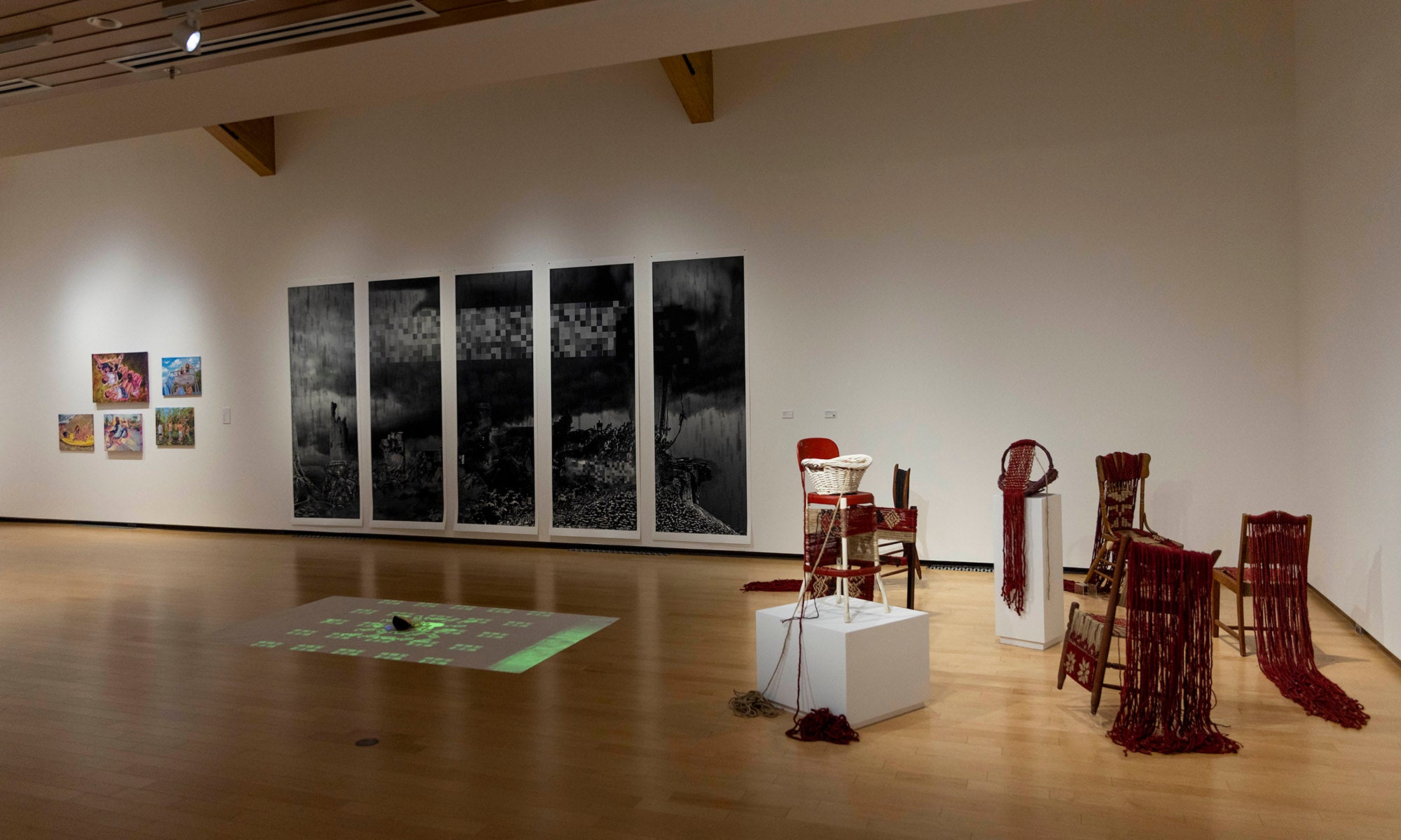 A contemporary art exhibition at Denison Museum features various artworks, including a series titled "It Was Never Just Then," large black-and-white panels, vibrant small pieces, and a striking floor installation with red and white objects.