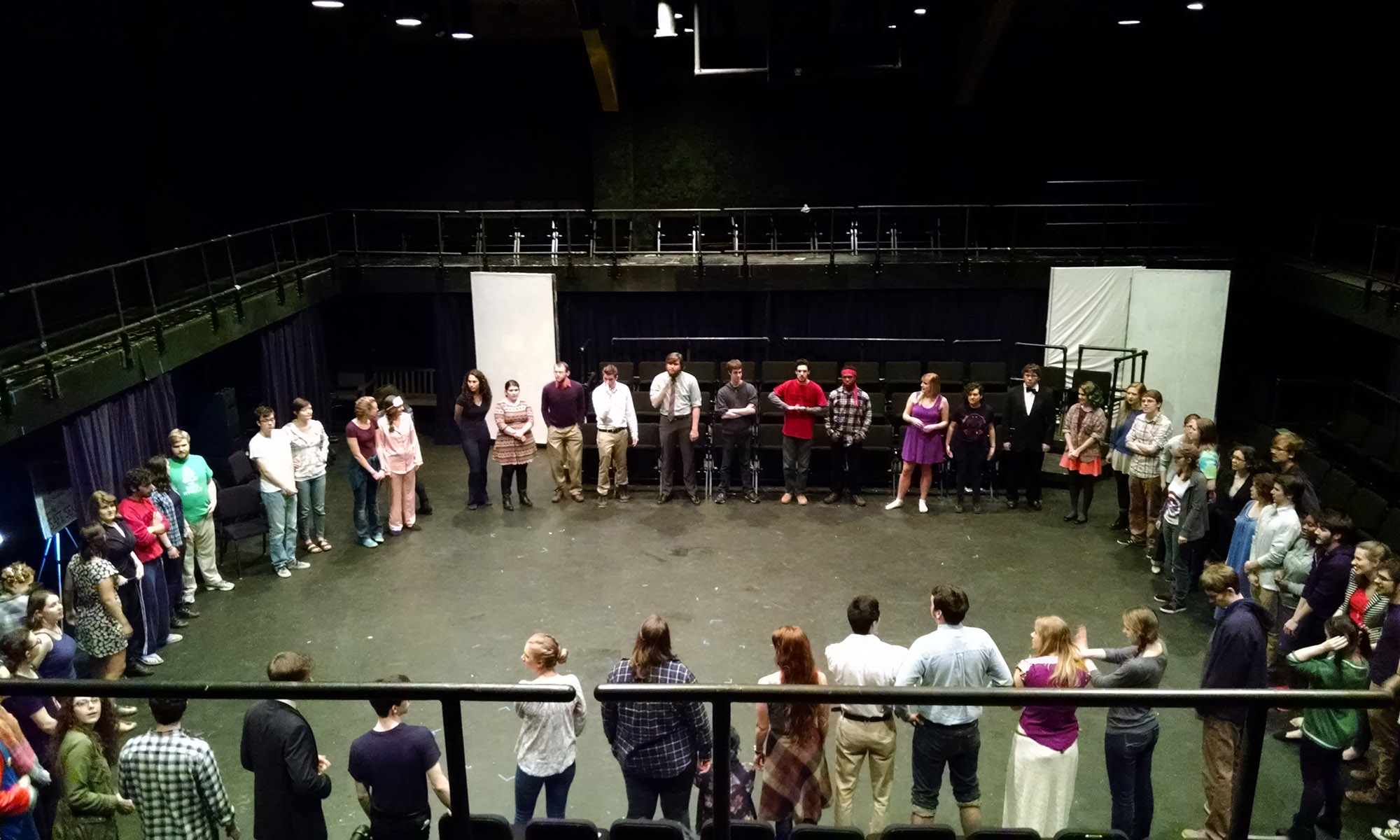 A large group of people standing in a circle on a theater stage.